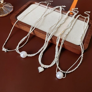 Détail de colliers de perles superposés avec pendentifs cœur argentés sur un plateau