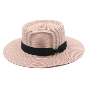 Detail view of pink straw boater hat with fine woven texture and black ribbon bow