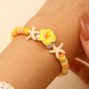 Primer plano de pulsera playera con cuentas Heishi amarillas, flores plumeria y estrellas