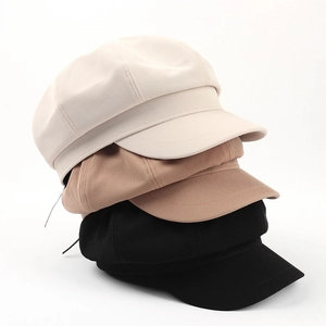 Tre cappelli newsboy in cotone nei colori beige, kaki e nero impilati su sfondo bianco