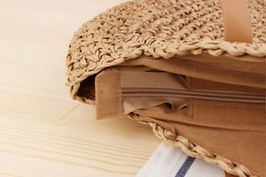 Close-up of circular straw beach bag featuring zipper closure and detailed woven texture