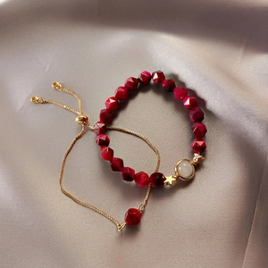 Deep red beaded bracelet set with gold star pendant on elegant grey silk background