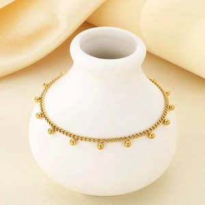Detail of a gold stainless steel chain bracelet with small beads on a white vase