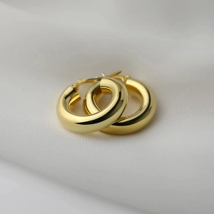 Close-up of chunky gold hoop earrings with mirror polish on white silk fabric