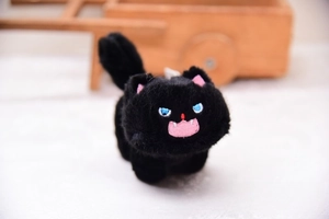 Close-up of black plush cat keychain with blue embroidered eyes and soft texture details
