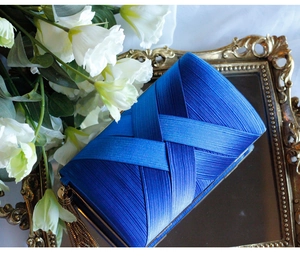 Close-up of royal blue satin pleated evening clutch with elegant gold fringe on a mirror tray