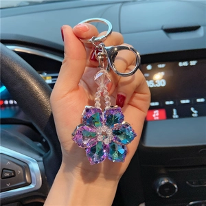 Detail of hand holding a crystal flower keychain with purple faceted petals in a car
