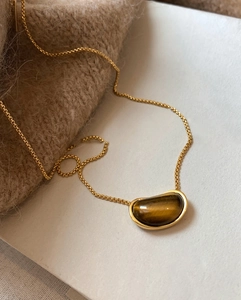 Macro detail of 18k gold plated tiger eye pea pendant on knitted sweater background