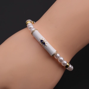 Detail of beaded evil eye bracelet with white pearls and gold accents on a wrist