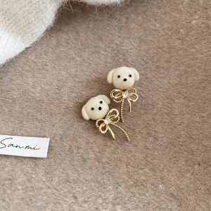 Macro detail of white flocked puppy earrings with gold bows and sparkling crystals