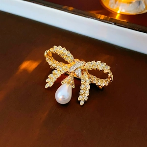 Vue latérale macro d'une broche nœud dorée avec cristaux et perle blanche en goutte