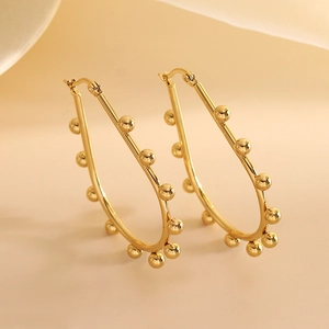 Detail of gold hoop earrings with small beads and polished geometric metal surface