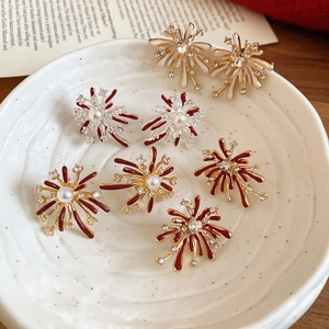Close-up of enamel firework stud earrings with pearls and crystals on a white ceramic plate