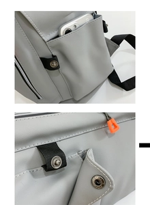 Detail of light gray travel backpack showing side phone pocket and orange zipper pulls