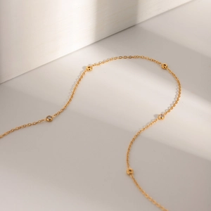 Elegant gold necklace featuring gold beads and clear gemstone beads on a white surface
