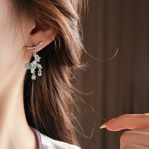 Detail of silver bow earrings with green butterfly zircon and long tassel on a model
