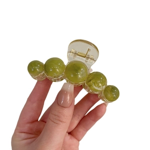 Hand holding a green gradient spherical claw clip made of textured plastic material