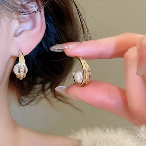 Detail view of gold C-shaped pearl earring featuring pavé cubic zirconia accents