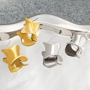 Artistic gold and silver irregular twisted metal earrings on a glass tray with mirror finish