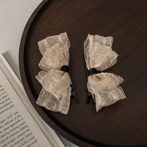 Detail of cream organza bow hair clips on dark wood tray with vintage book background