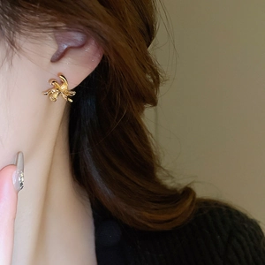 Close-up of elegant gold twisted knot stud earring worn on ear with metallic luster