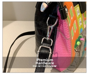 Close-up of silver metal hardware, embroidery, and croc-textured leather on handbag