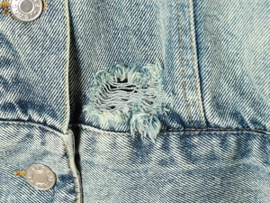 Close-up of light blue washed denim jacket with distressed ripped details and metal buttons