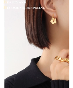 Detail of gold flower earrings and geometric rings worn by a model in soft lighting