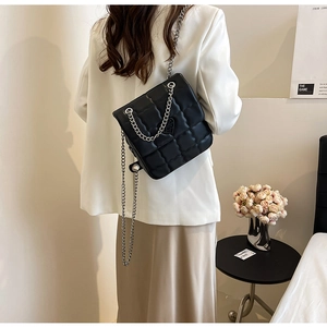 Close-up of black quilted chain bag on model showing square texture and silver strap
