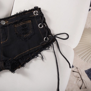 Dettaglio di pantaloncini in denim nero a vita bassa con lacci laterali e bordi sfrangiati