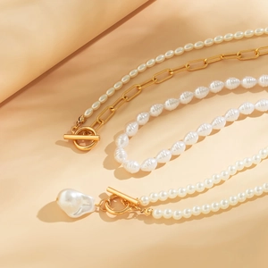 Detailed view of baroque pearl necklace set with gold OT clasp on beige fabric