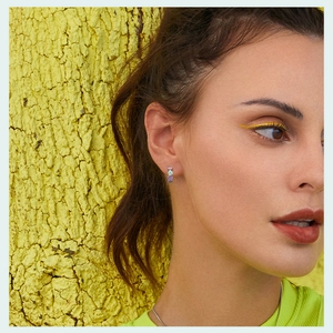 Close-up of model wearing colorful gemstone earrings with pink, blue, and green stones