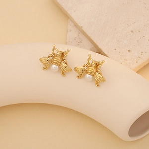 Detailed view of gold bee stud earrings featuring white pearls on stone background