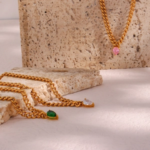 Macro detail of gold Cuban chain necklaces with pear-cut pink, green, and white gemstones