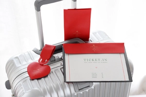 Macro detail of a red leather passport holder and heart luggage tag set on suitcase