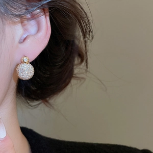 Close-up of gold plated round stud earring with pavé zircon crystals on ear model