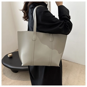 Minimalist beige faux leather tote bag being carried by a model in a modern room setting