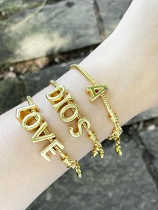Close-up of three gold-plated letter bracelets featuring A, LOVE, and DIOS pendants