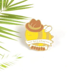 Gros plan du pin's émaillé BEEHAW avec une abeille en chapeau de cow-boy sur fond blanc