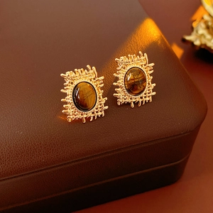 Detail of vintage gold tiger eye earrings with woven metal texture on brown leather