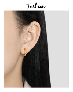 Detail of twisted gold-plated titanium hoop earrings worn on ear with polished finish