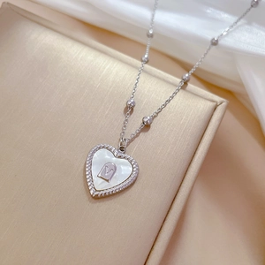 Macro shot of silver heart shell pendant with V-letter inlay on gold textured surface