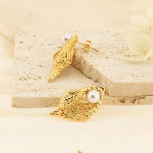 Détail de boucles d'oreilles dorées géométriques irrégulières avec incrustation de perle