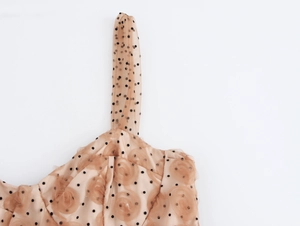 Dettaglio di abito elegante a pois con rose in rete 3D e spalline sottili color albicocca