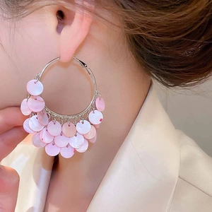 Close-up of model wearing geometric large hoop earrings with layered pink shell charms