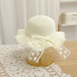 Détail d'un chapeau de paille beige avec un grand nœud en dentelle et motifs cœurs