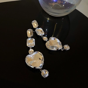 Macro shot of oversized crystal heart earrings with tiered rectangular stones on a mirror