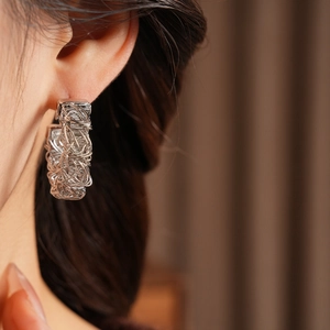 Close-up of geometric wire-wrapped silver earrings showing woven metal texture on a model