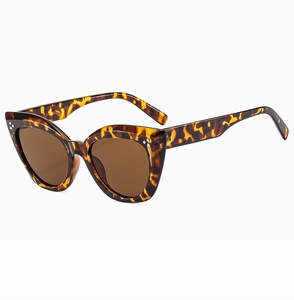 Detail view of tortoiseshell cat-eye sunglasses with metal rivet accents and brown lenses