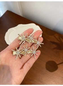 Close-up of hand holding two gold star-shaped hair clips with sparkling rhinestones